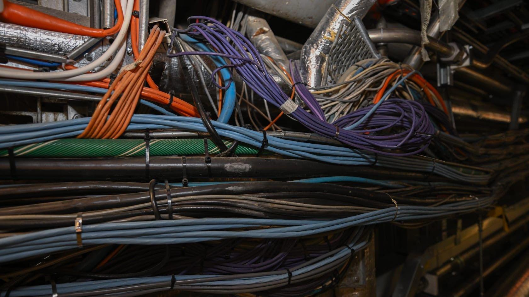 Disa grupe telash me ngjyra të ndryshme që kalojnë përgjatë një korridori. Disa prej telave mbështillen rreth të tjerëve ose rreth njërit prej tubave.