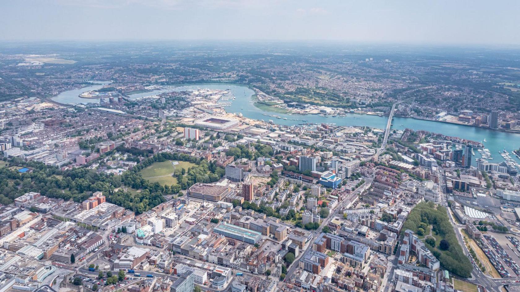 An aerial view of Southampton city centre. You can see buildings and parks with the River Itchen running through the picture. Near the river you can see St Mary's stadium and the Itchen Bridge. 