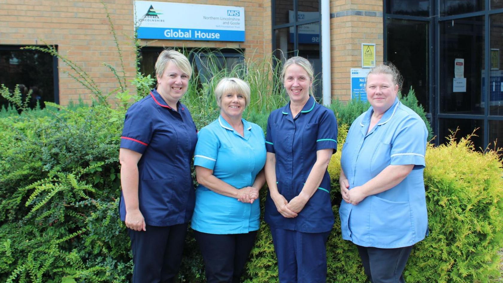 Four members of the community inclusion team standing alongside each other in a row outside a sand-coloured brick building in Scunthorpe. They are wearing blue and navy uniforms while smiling and looking directly at the camera.