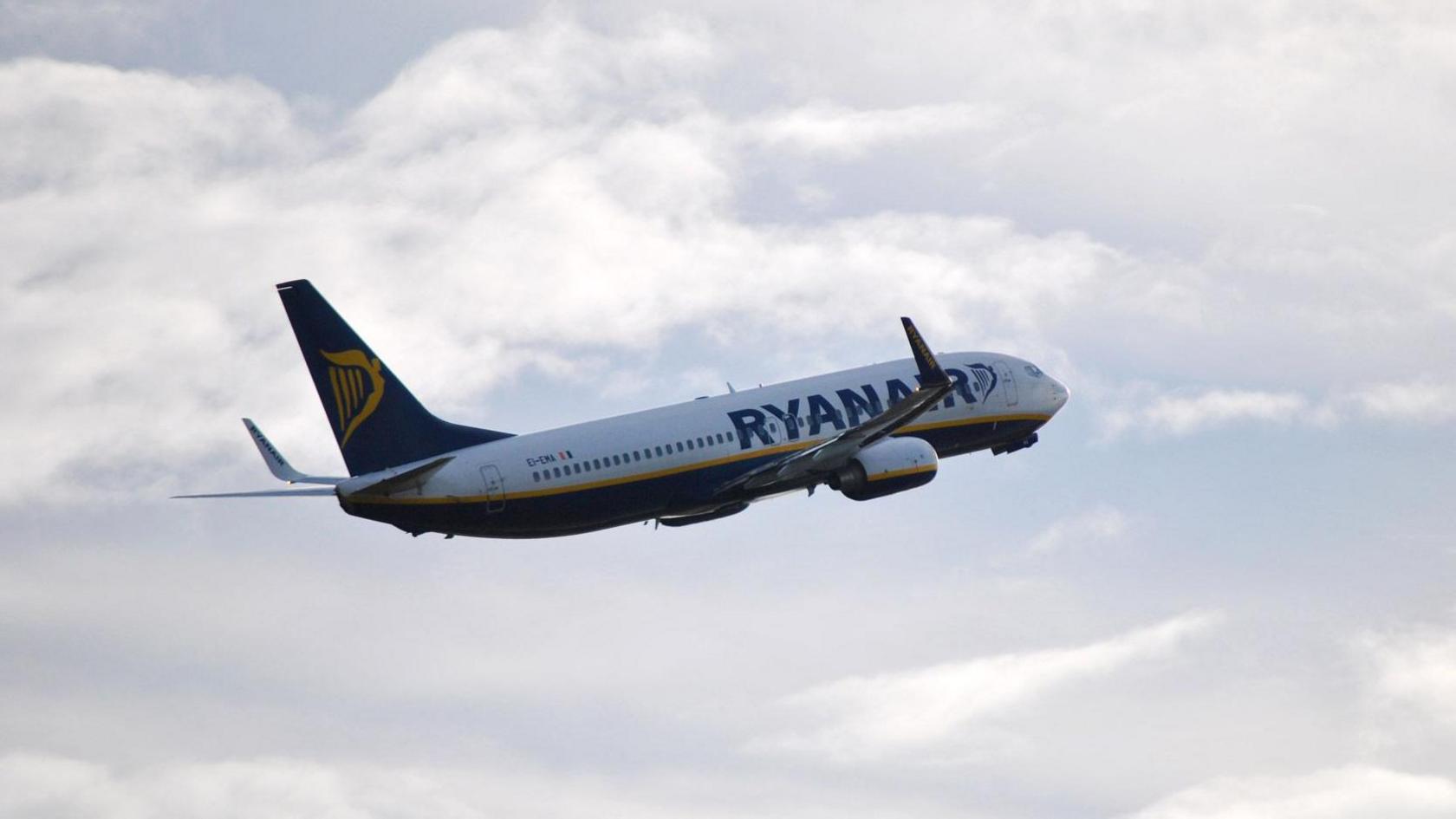 A Ryanair aeroplane mid flight against a cloudy sky.
