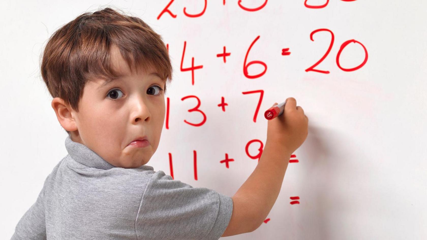 A boy completing sums on the whiteboard looking confused