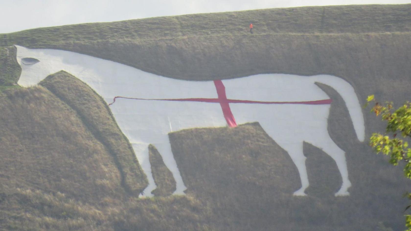 The Westbury White Horse, a white chalk figure on the hillside, with a red ribbon on top to create an English flag.