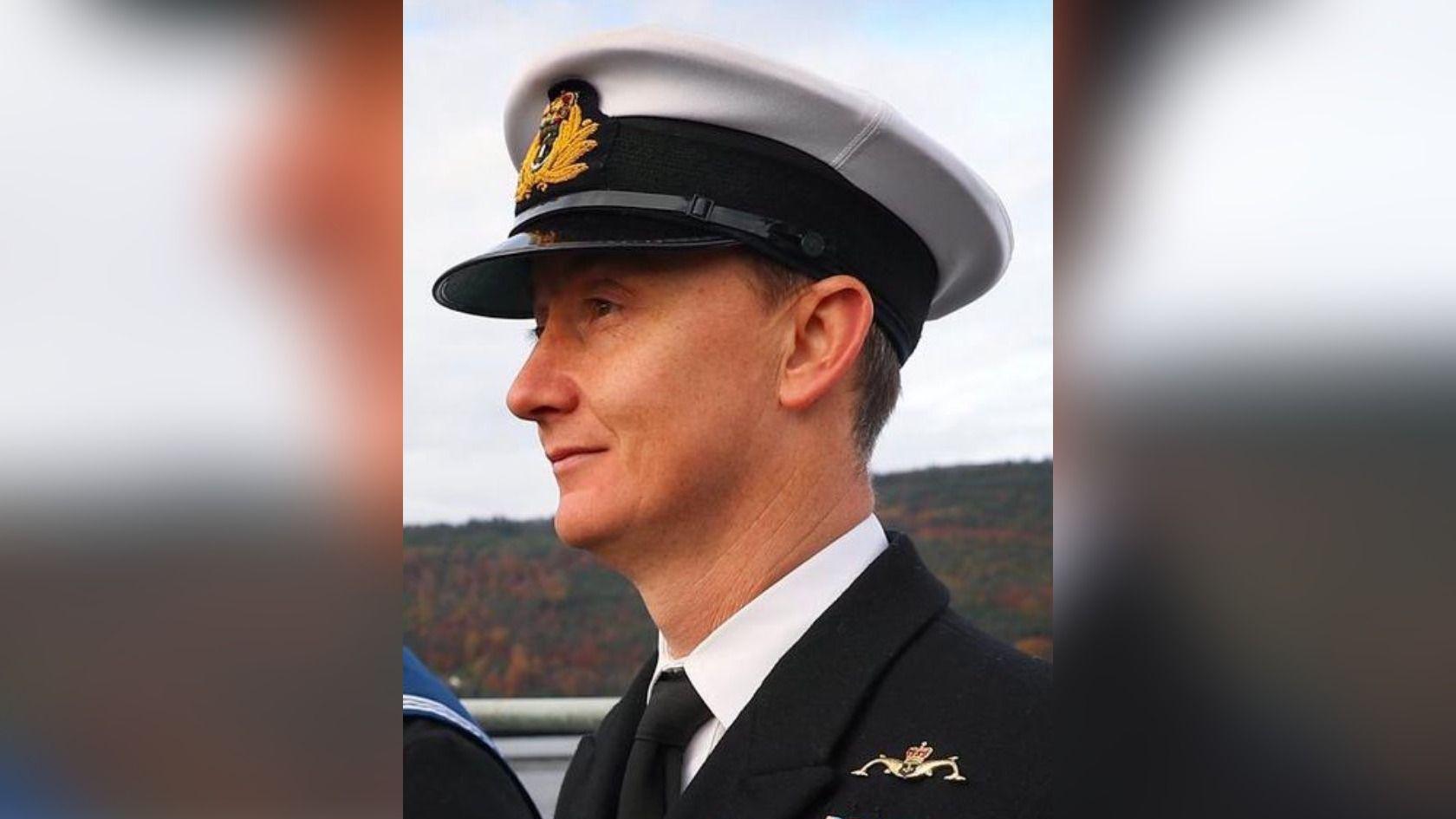 A head-and-shoulders photo of Lieutenant Commander Alex Mills man wearing Navy uniform, including a naval hat and a tie.