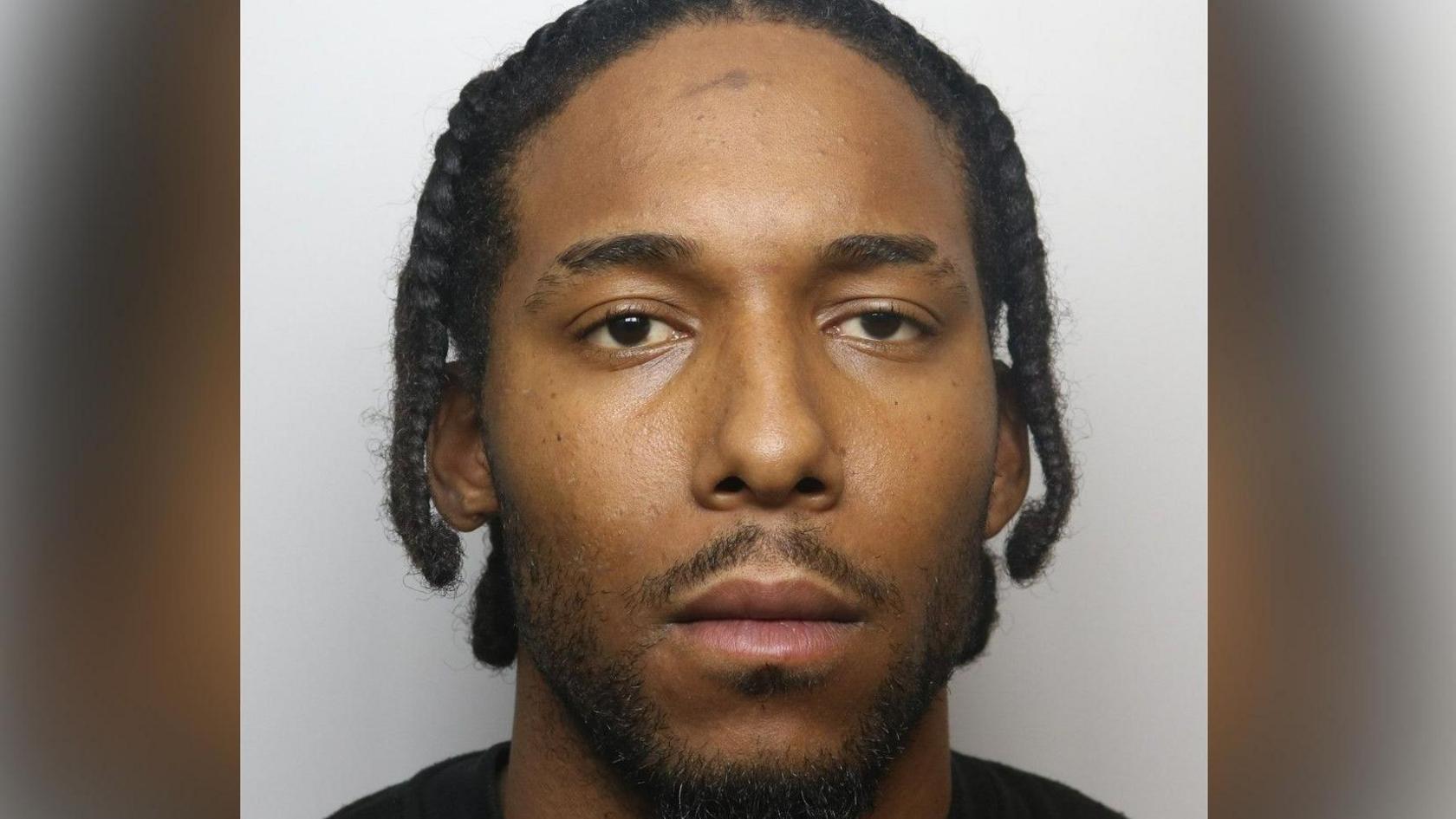 A police mugshot of Rajae Paul, who has braided hair and brown eyes. He is staring directly at the camera.
