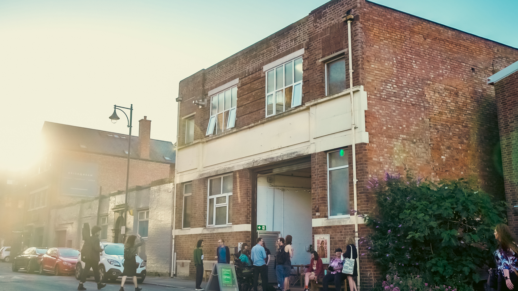 Artists sitting and standing outside the gallery - a two storey brick building/warehouse