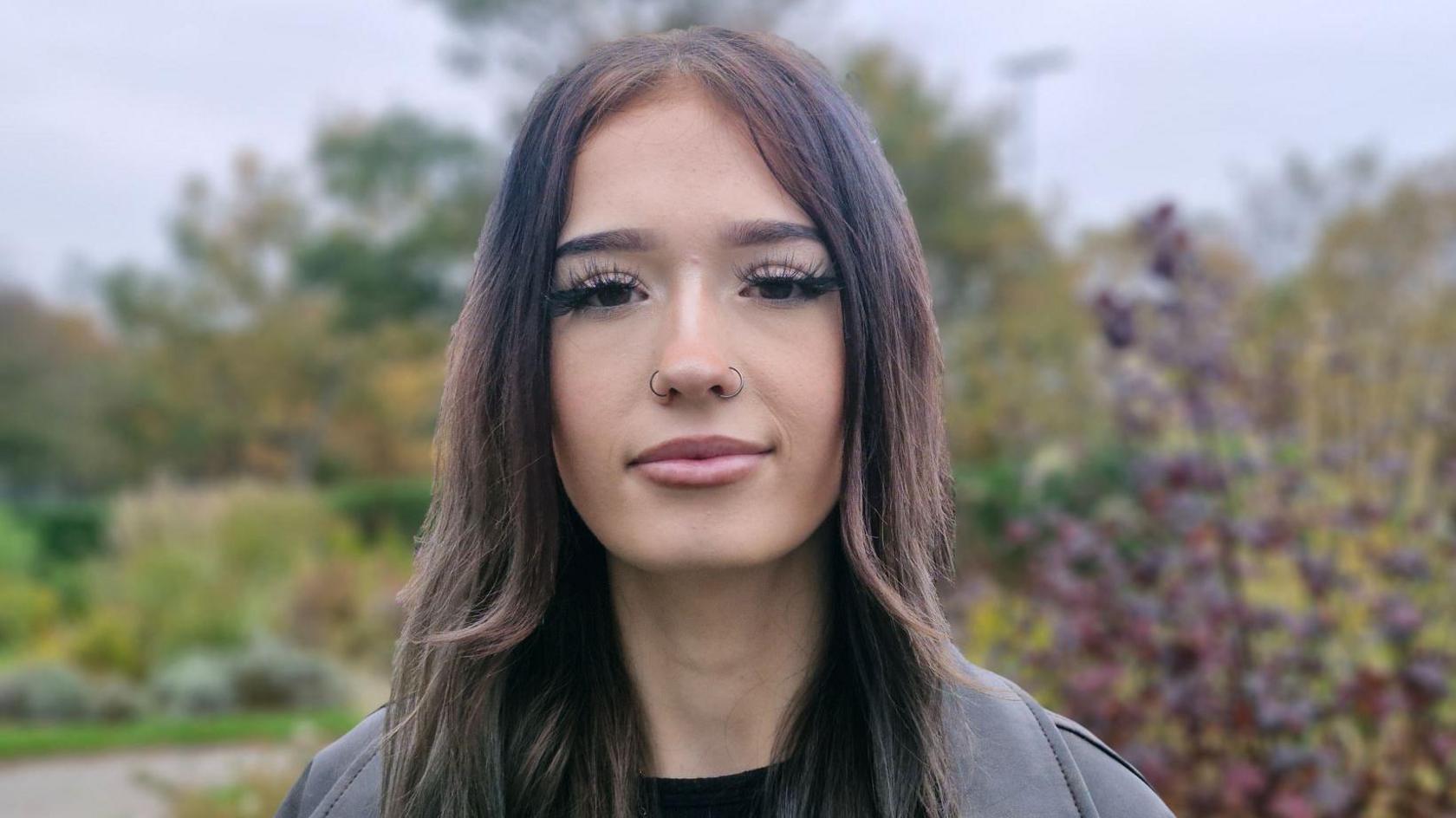 Kallie had long dark hair and two nose rings. She is wearing a black leather jacket and a black top.