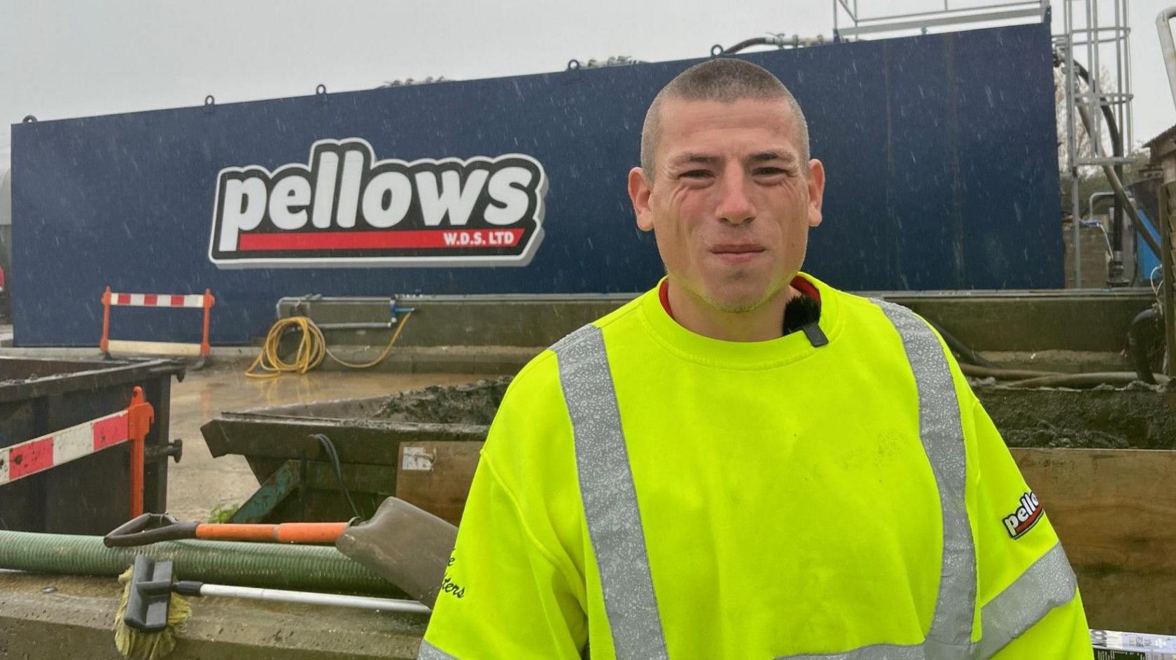 A man with a high viz  jacket stands in front of a large waste tank full of sewage. 