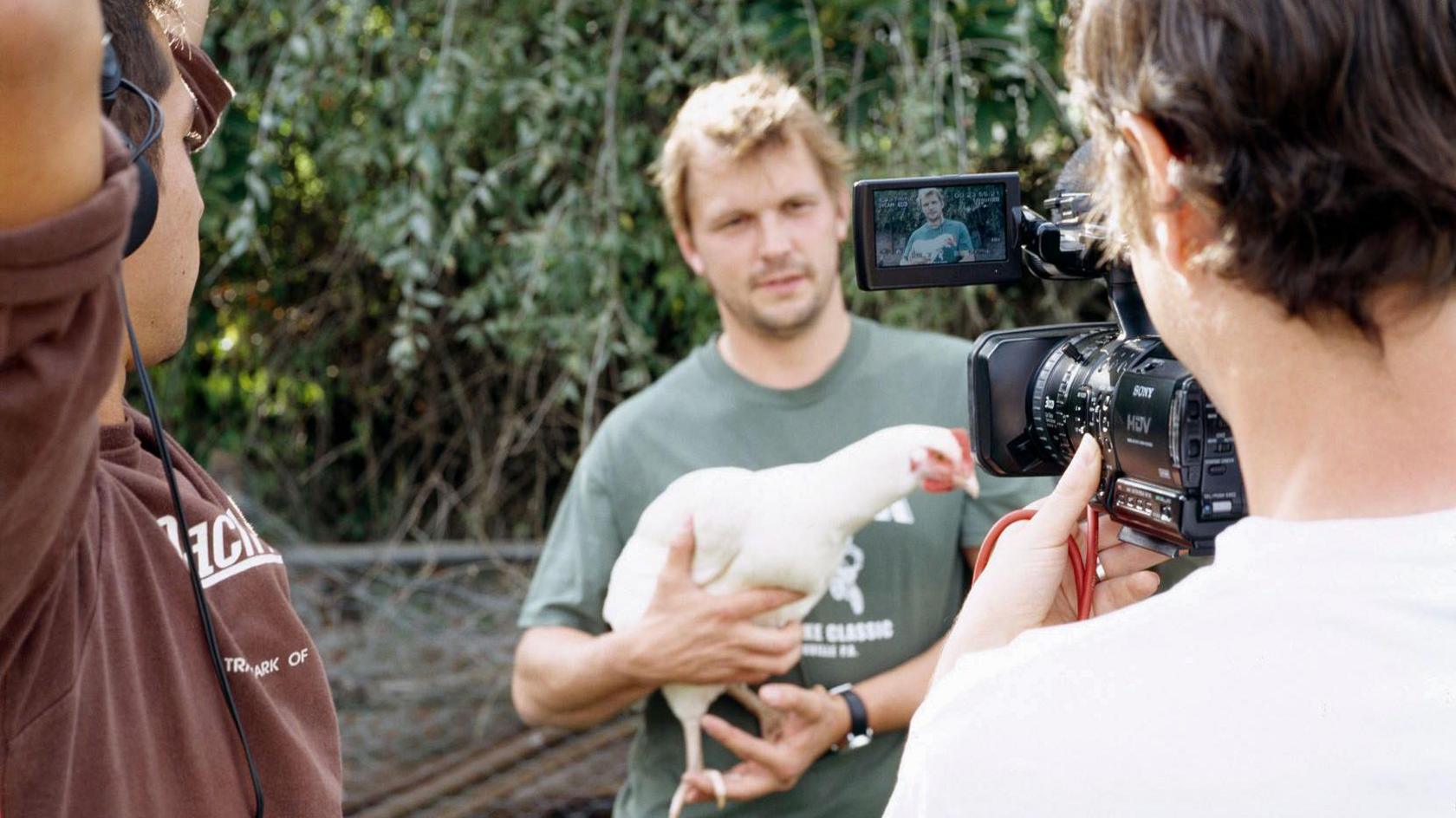 Jimmy Doherty holds a chicken in front of a TV camera.