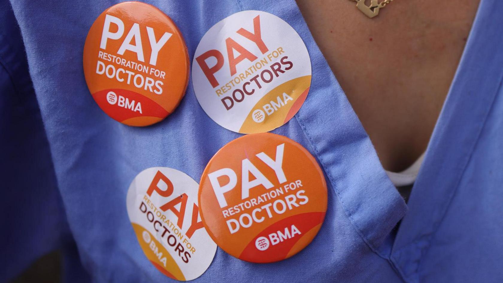 A pair of scrubs with four stickers that say 'pay restoration for doctors'