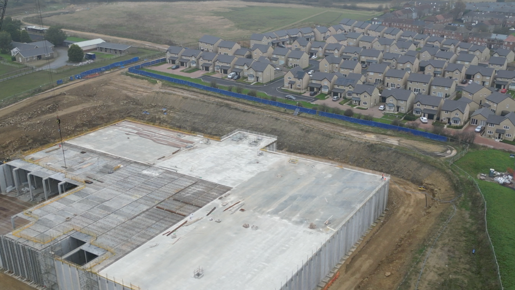 Aerial view showing a large concrete structure with banked earth walls around it, and a new housing estate beyond