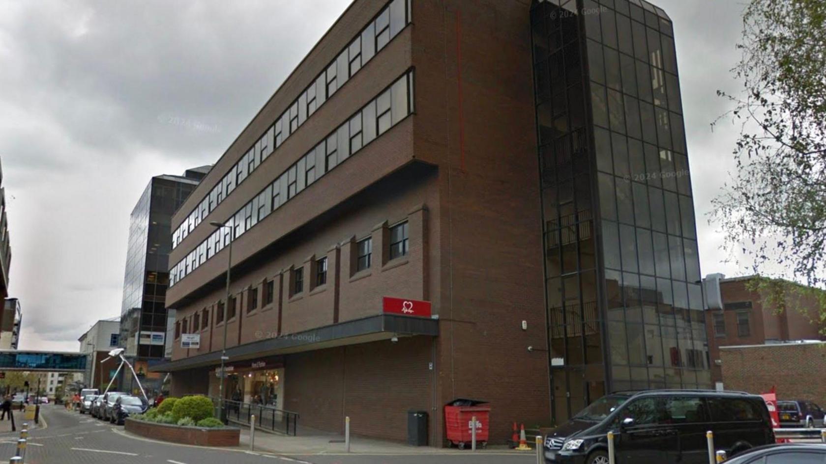 A Google Maps image of the former BHS site in Woking town centre. There is a large brown building with a road in front. 