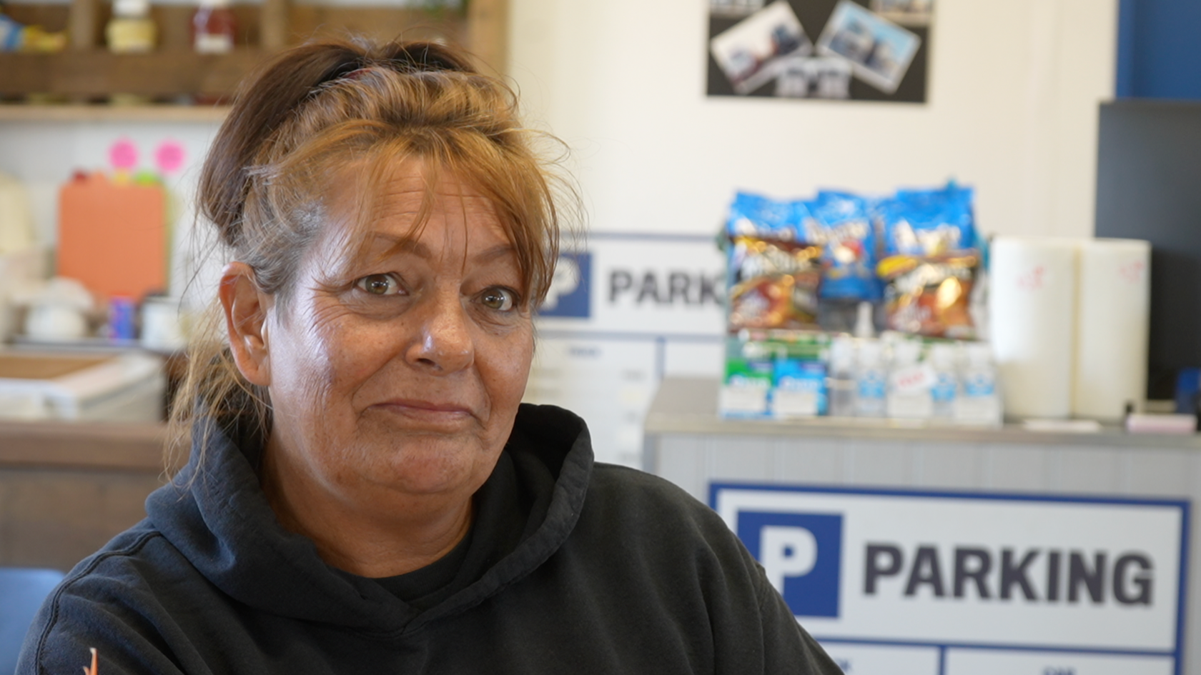 Woman sits inside truck cafe and looks at camera. She is wearing a navy hoodie and her hair is tied back.