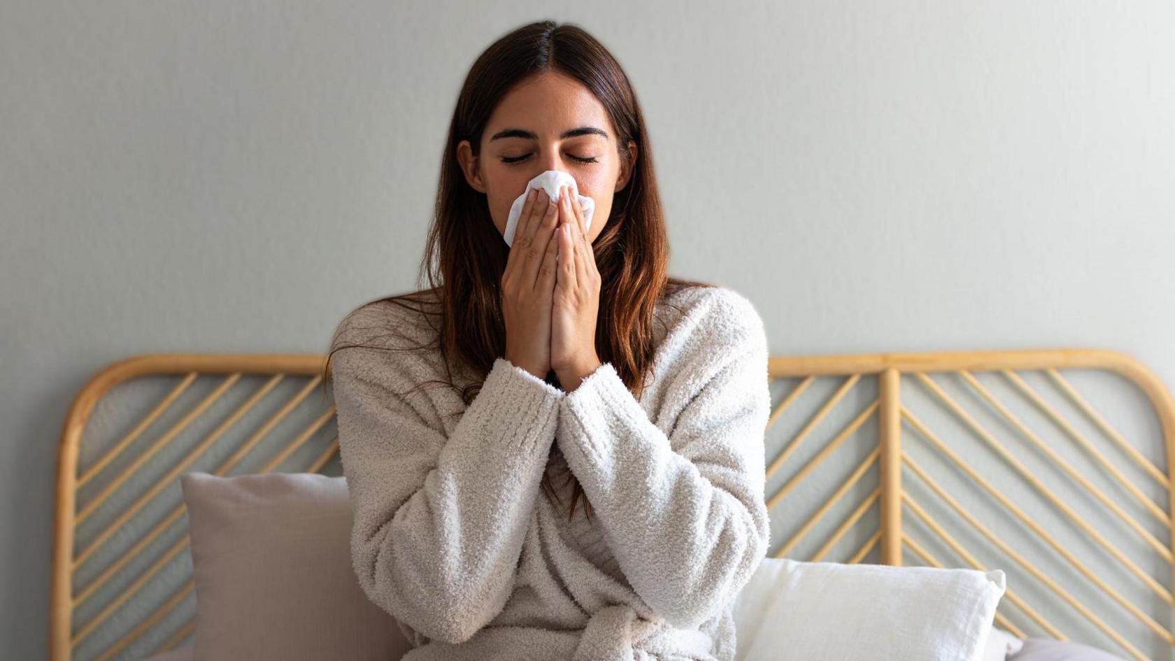 Young woman blows her nose in bed 