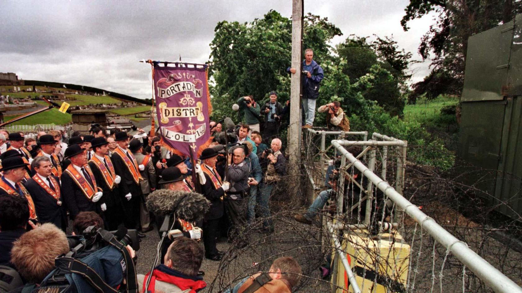 A group of Orange Order members standing at a fence in the middle of a road. 