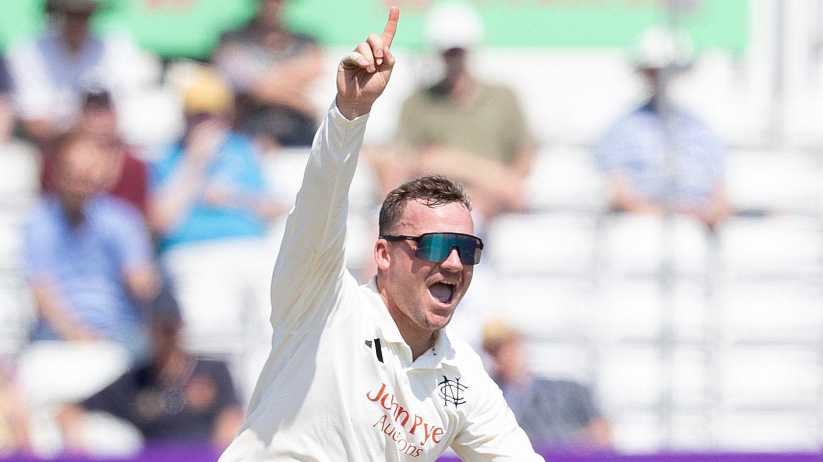 Liam Patterson-White celebrates taking a wicket by raising his right hand with his index finger pointing towards the sky.