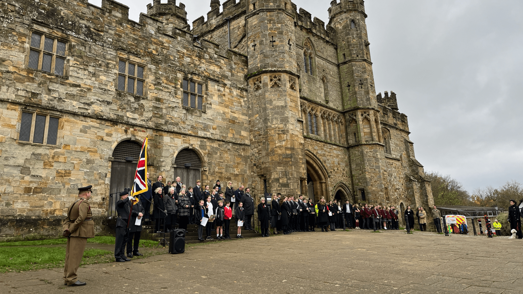 People gathered with flags and wearing military uniforms outside Battle Abbey.
