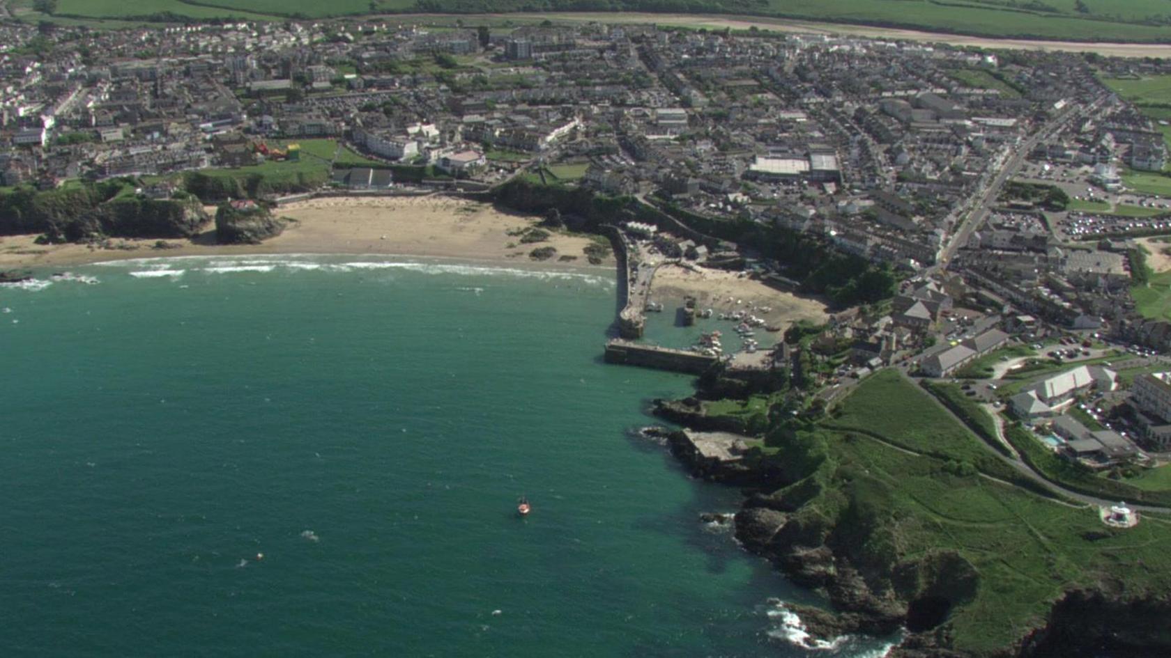 Aerial shot of a seaside town with harbour and beaches and houses stretching inland.