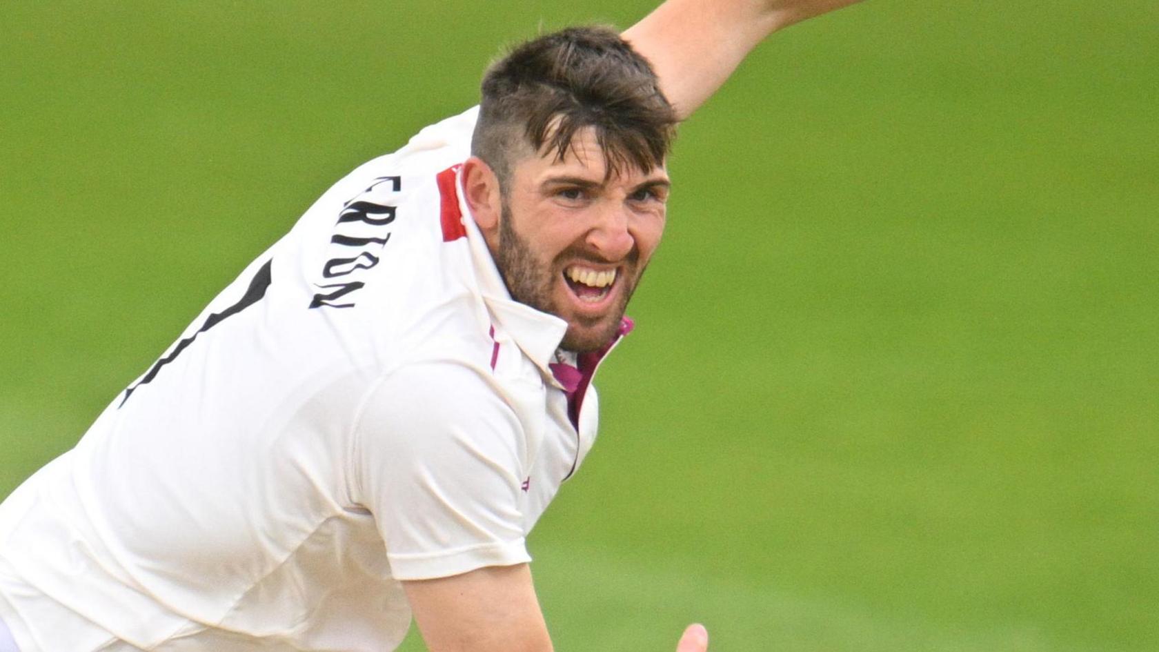 Craig Overton in cricket whites bowls with a grimace