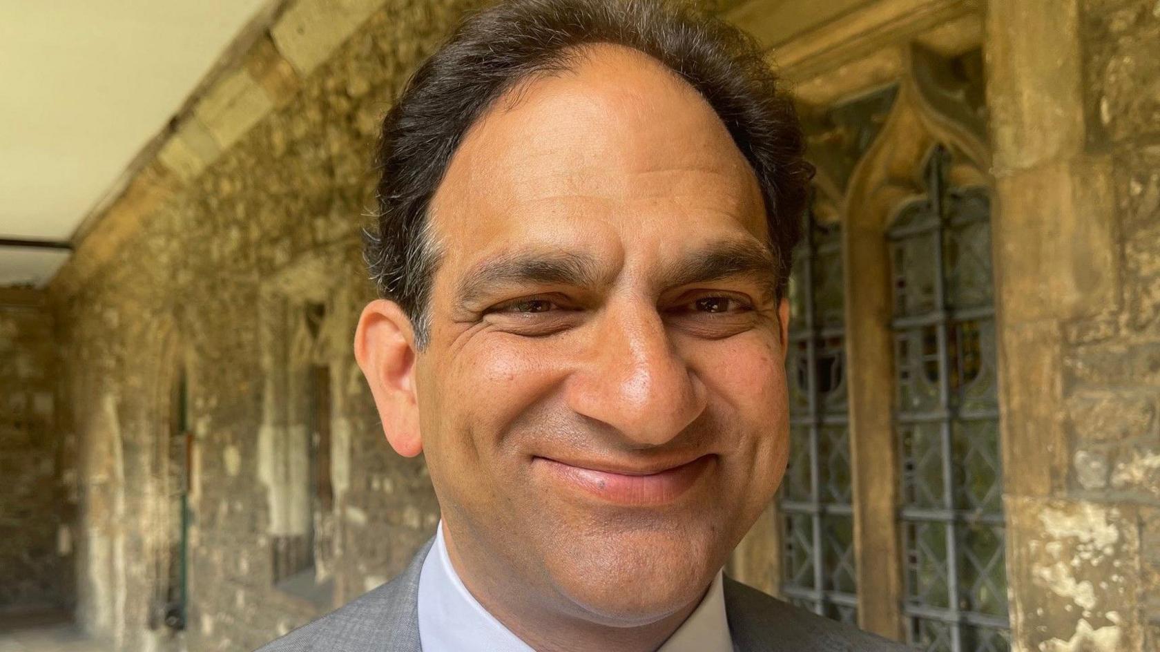 A man smiles into the camera from the cloisters of Westminster Abbey