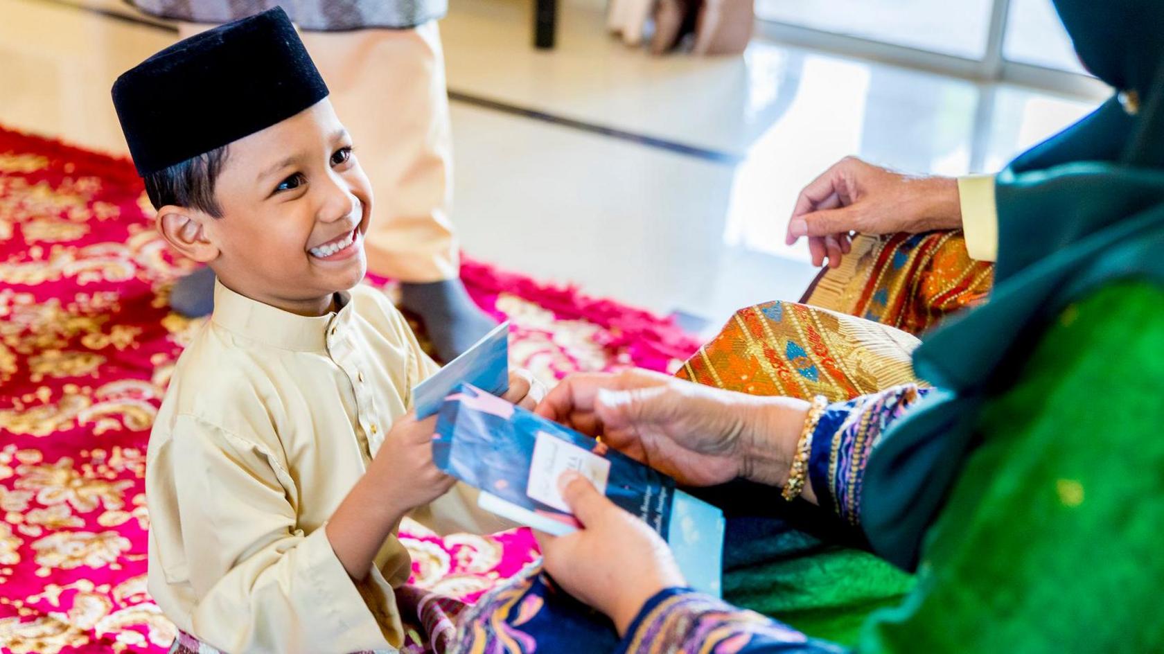 Family celebrating Hari Raya Aidilfitri, showing a grandchild being handed Duit Raya by his grandmother.