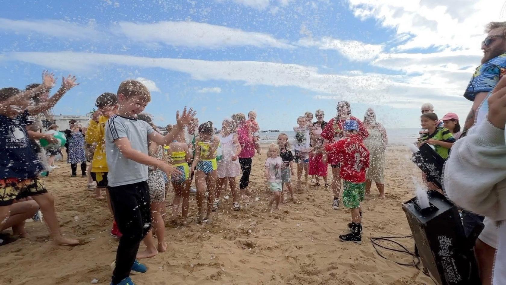 Children play in front of a snow machine on the beach