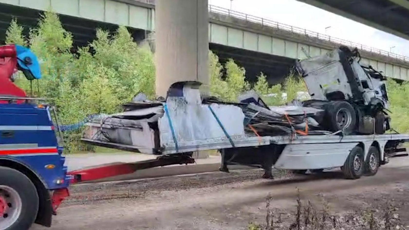 A lorry being towed away by a recovery truck after it fell off a motorway bridge on to an embankment