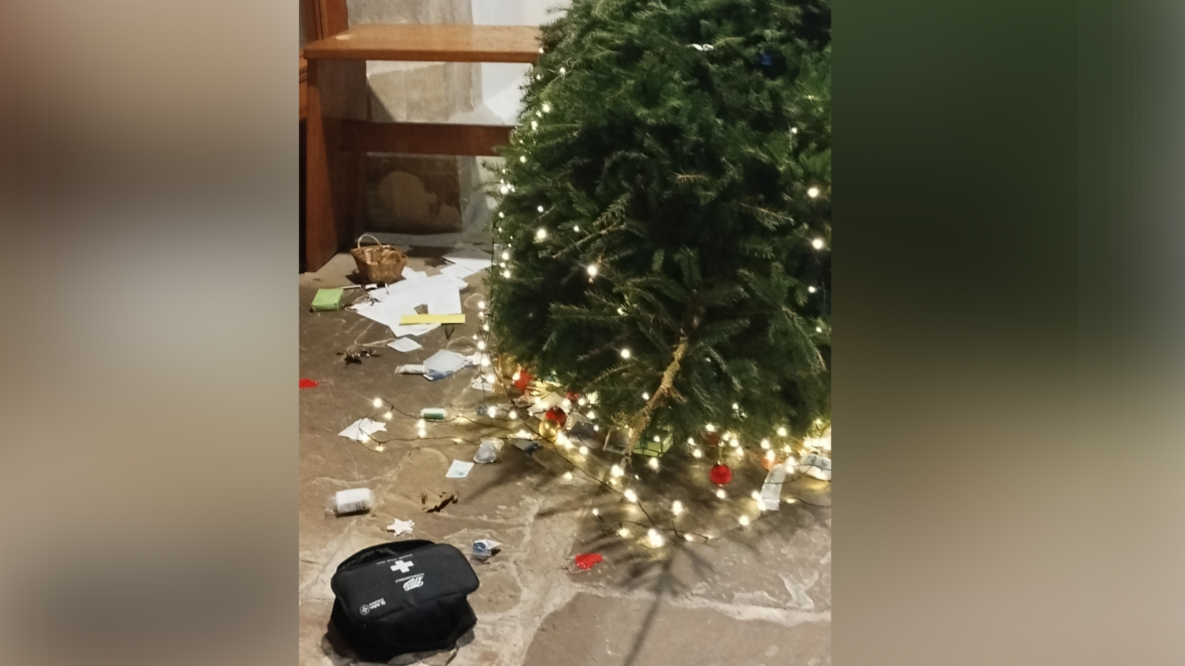 A Christmas trees lies horizontally on the floor of a church after it was torn down. A black first aid box sits next to it as well as decorations that have fallen off.