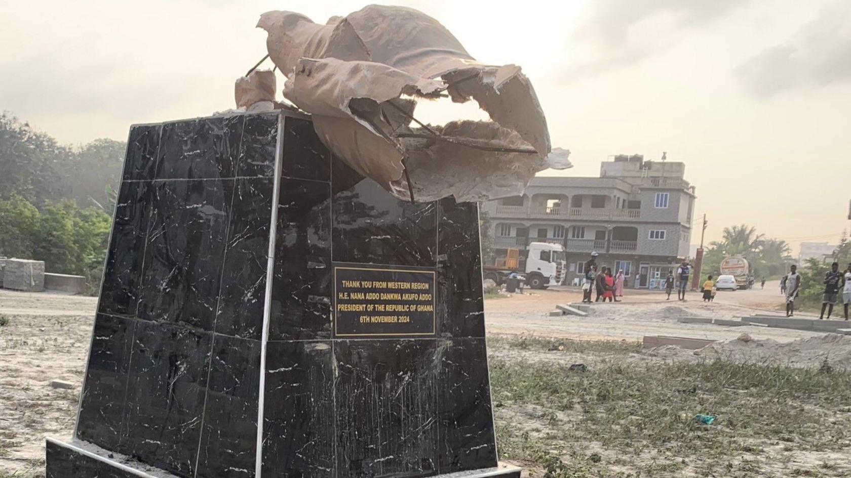 A pedestal on which the statue of Nana Akufo-Addo once stood. The words "Thank you from Western Region, H. E. Nana Addo Dankwa Akufo Addo, President of the Republic of Ghana, 6th November 2024" are inscribed on one side of the pedestal, black in colour, and part of the ruined statue on top