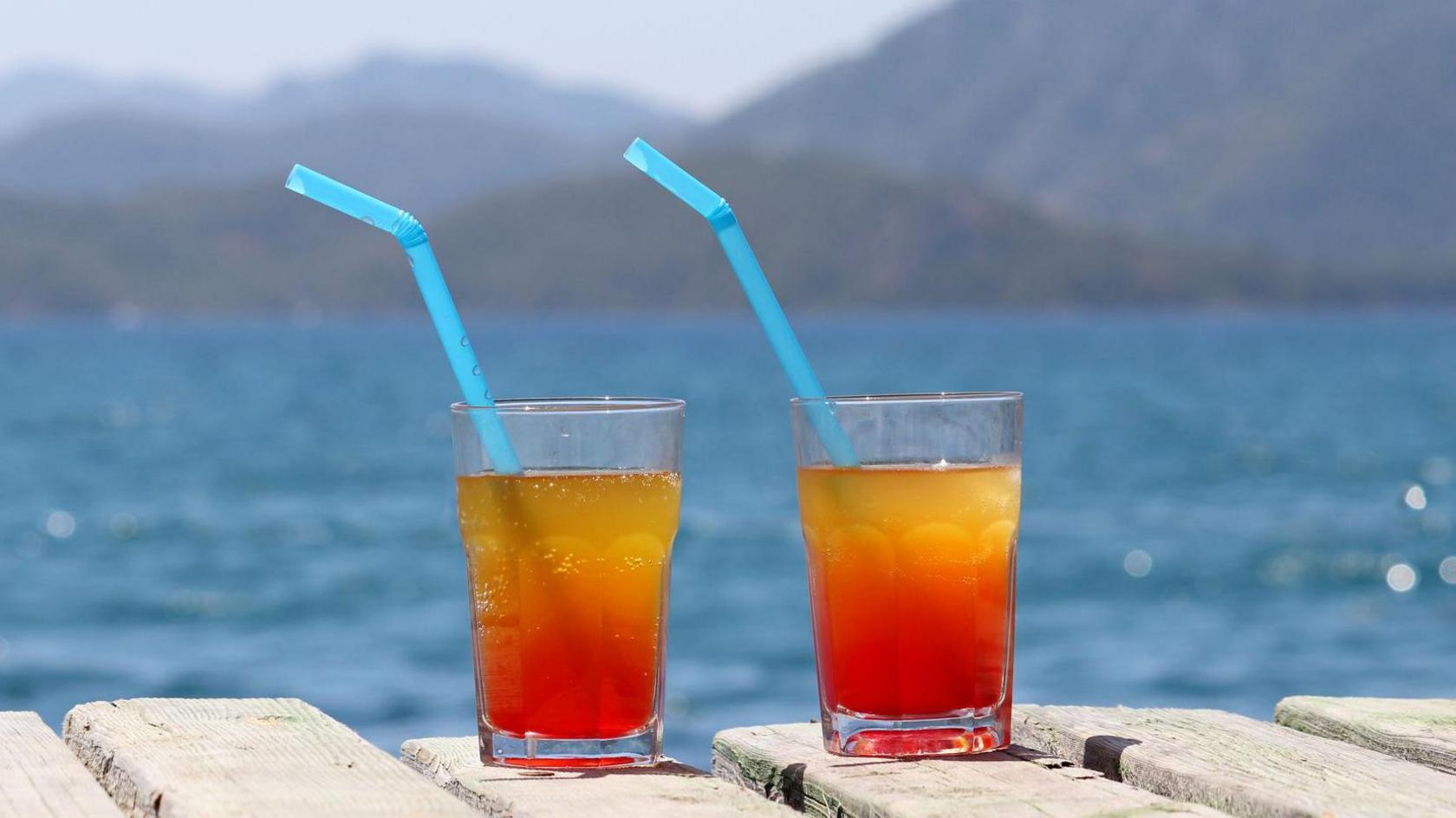 Two glasses with cocktail on a wooden pier on sea and mountains background