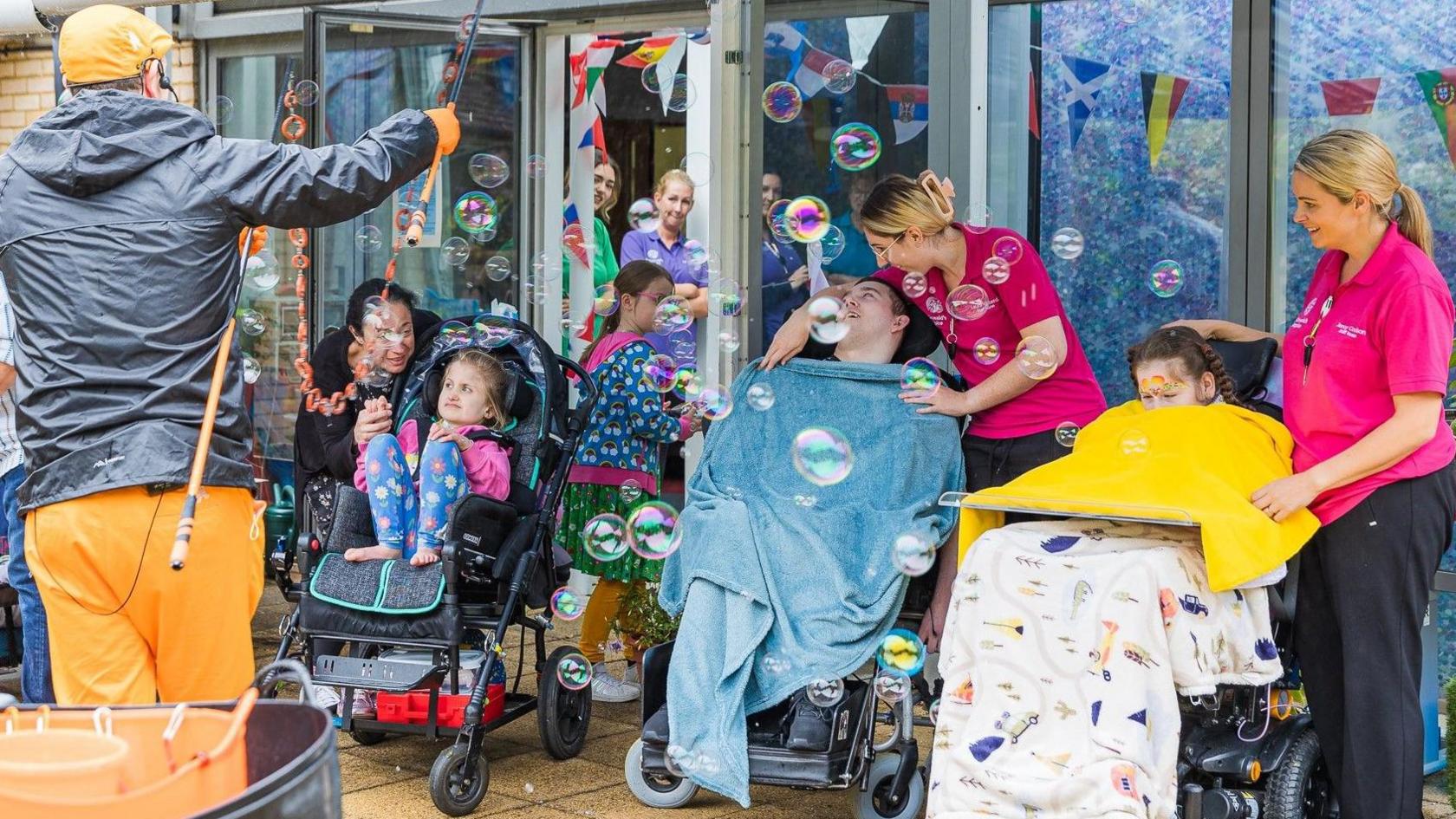 An entertainer in front of laughing children with extra needs in wheelchairs and pushchairs supported by carers