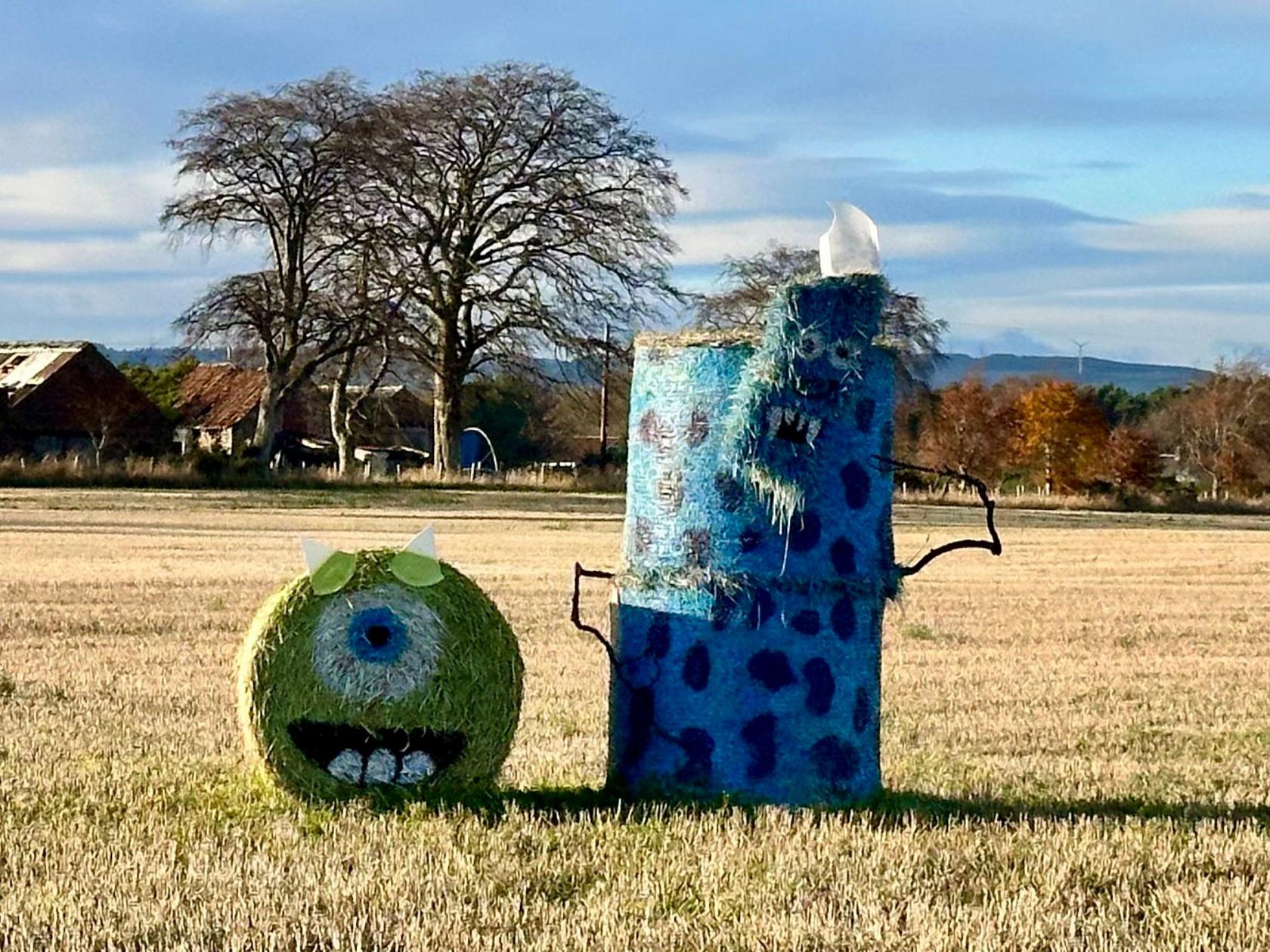 Two large hay bales with colourful faces drawn on the side of them in a farm field in Scotland.