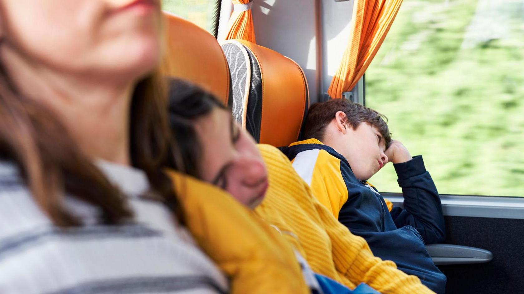 A back row of a coach where two children and an adult are trying to sleep.