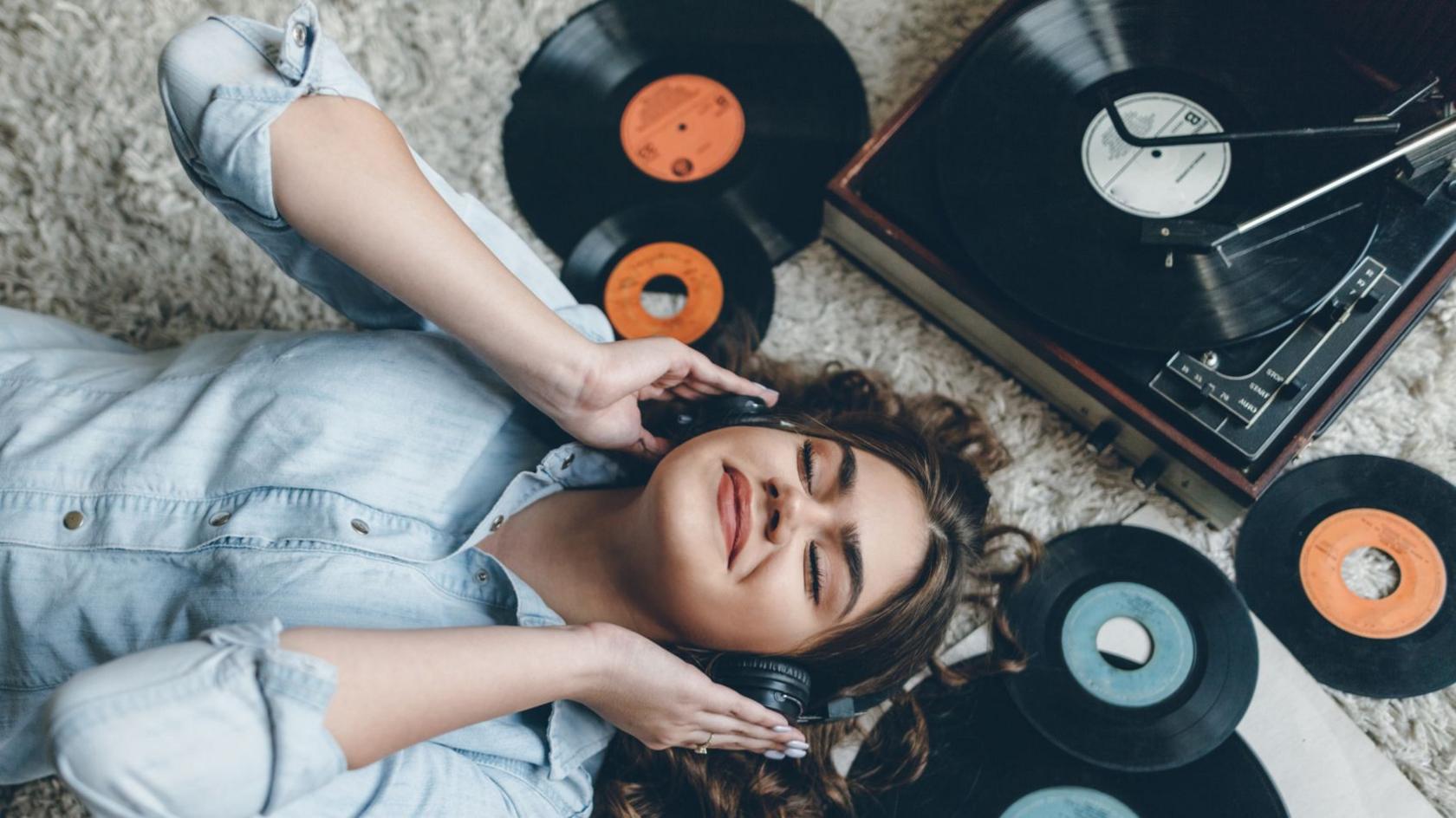 Woman lying on the floor, smiling as she listens to records.