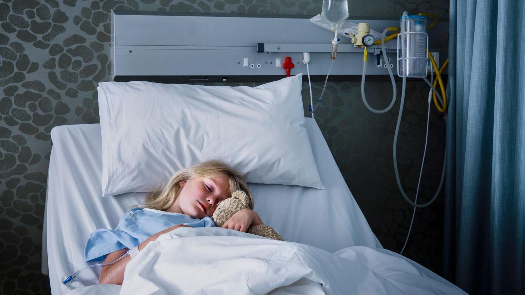 A little girl in a hospital bed sleeping with her Teddy Bear