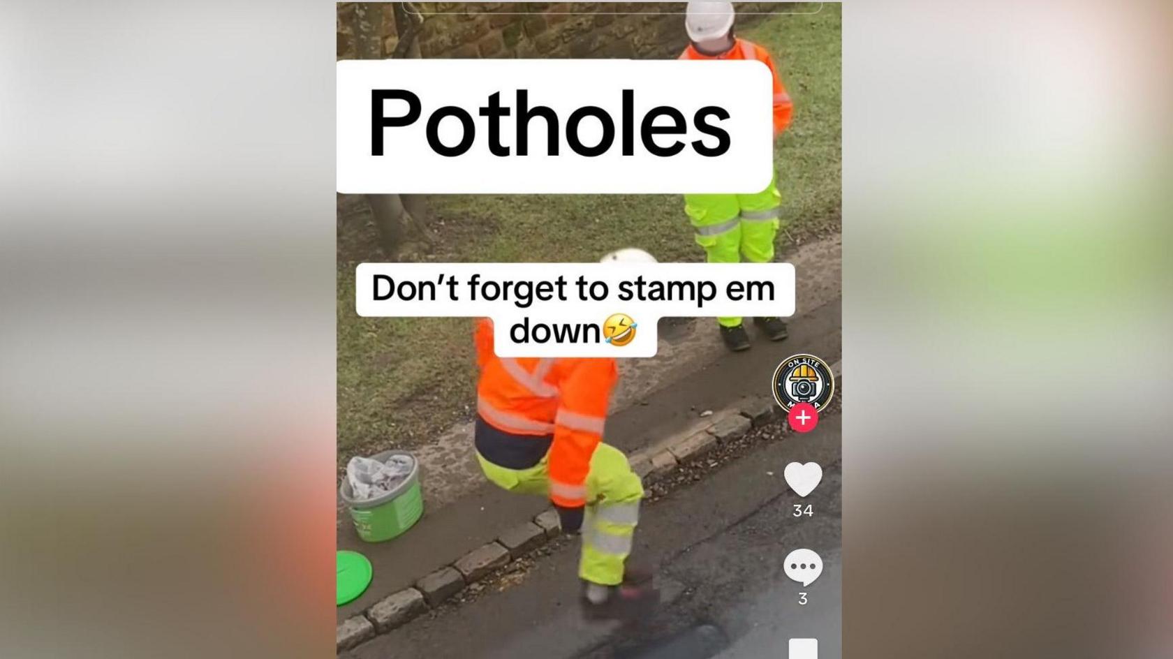 Two men in orange and yellow hi-vis with white helmets are at the side of a road on which a pothole has been filled. One is watching from the pavement while the other appears to be jumping on the pothole. Both feet are off the ground and his knees are bent.