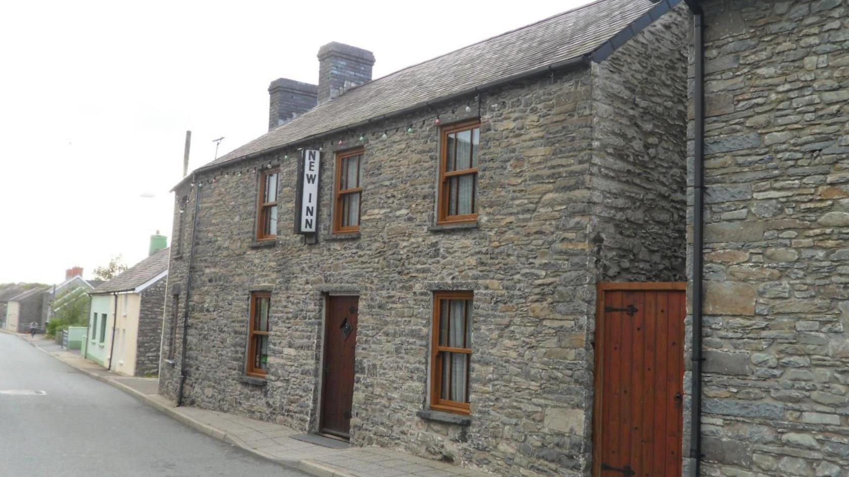 Llun o dafarn y New Inn ger ochr lon yn y pentref. Mae gan y dafarn oleuadau bach yn hongian uwchben ei ffenestri, sydd a phaneli pren coch-frown iddyn nhw.