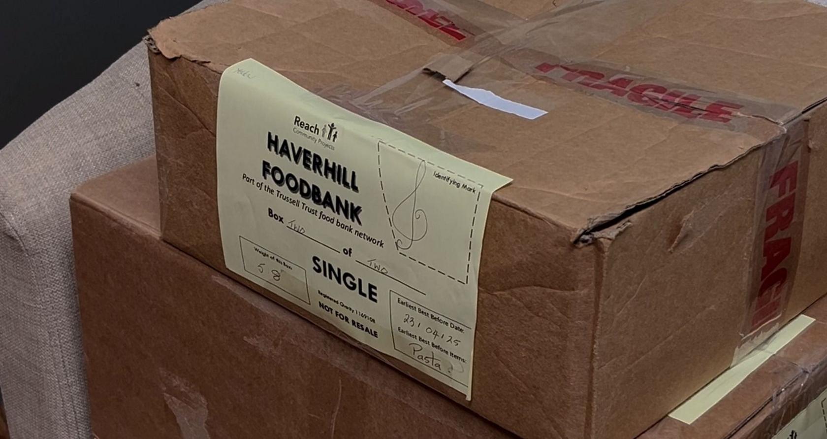 A cardboard box is pictured with a yellow sheet on paper on its front that reads Haverhill Foodbank