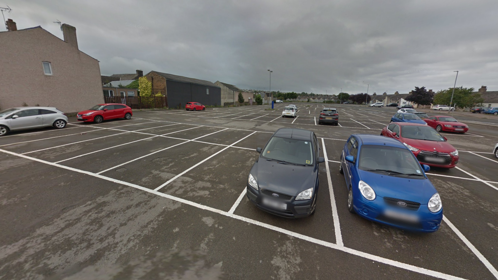 Central car park is a large, but sparse car park. There are houses and single-storey businesses surrounding the car park.