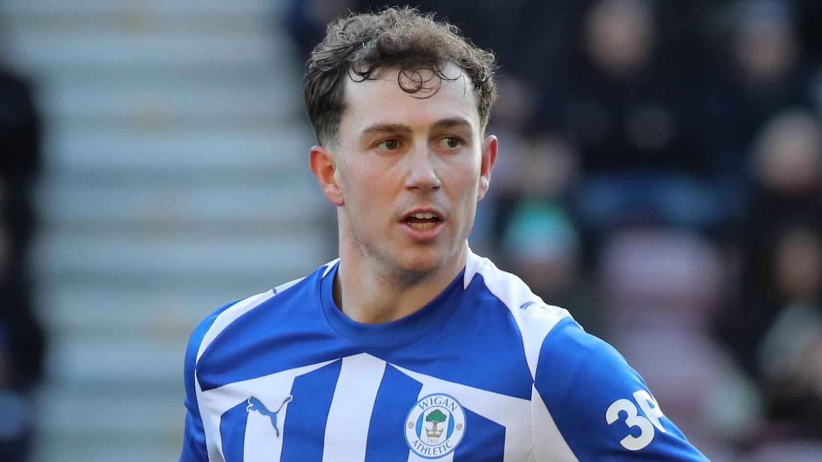 Jensen Weir, wearing Wigan's blue and white striped home shirt, in action during a game against Huddersfield Town