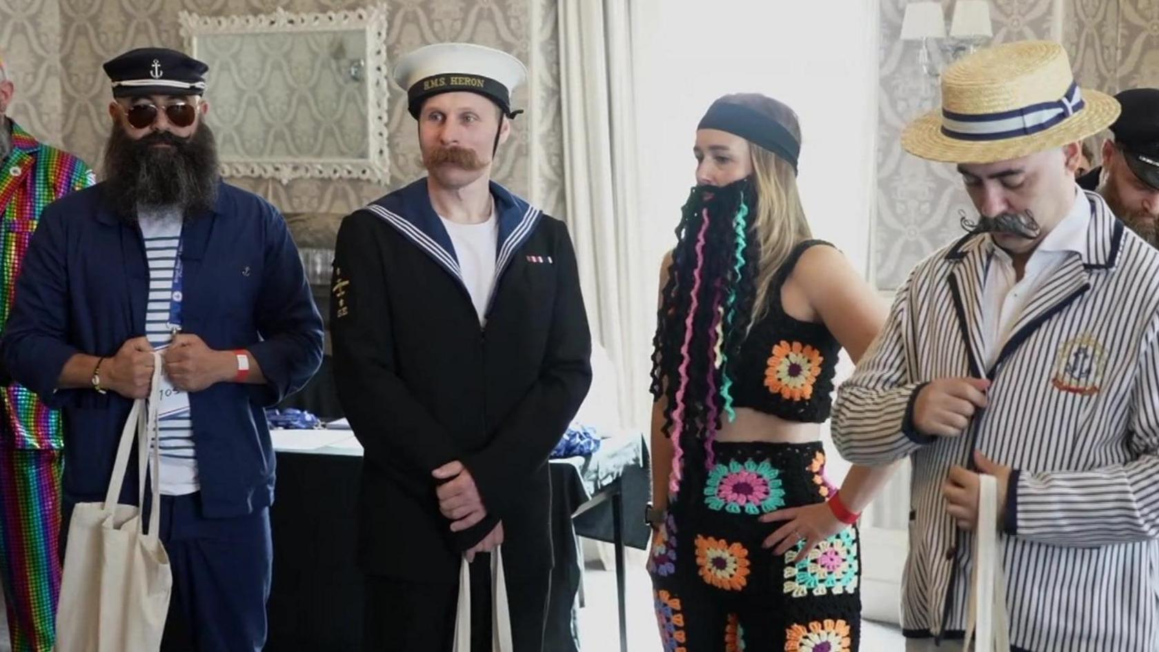 Four people stood in a line displaying their beards and moustaches