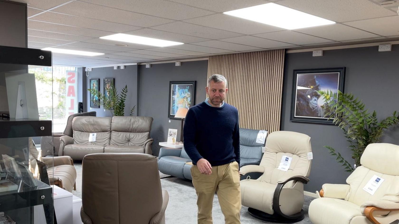 A man with a beard walks through a furniture showroom.