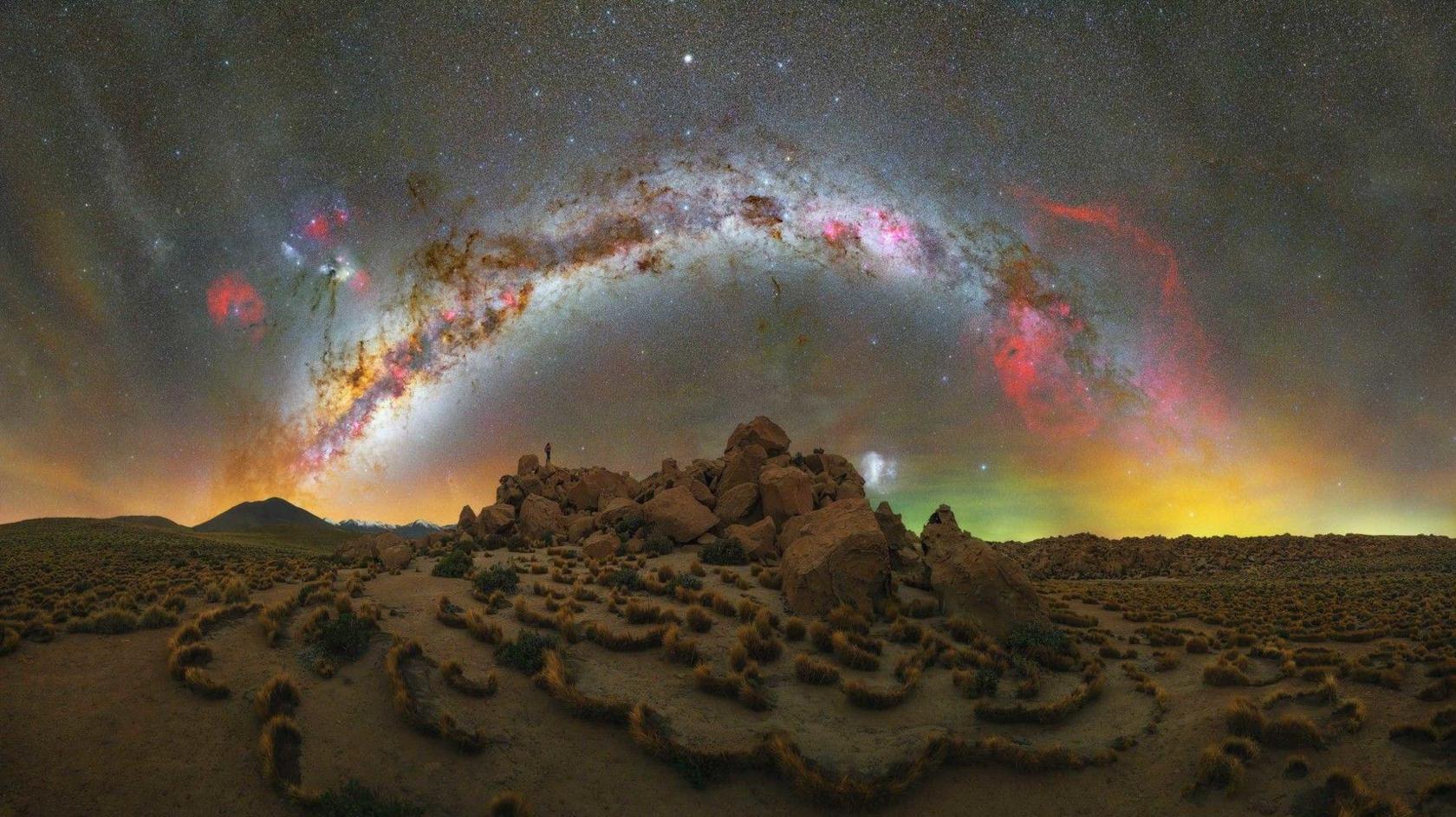 A desert with a rainbow coloured Milky Way arcing above it