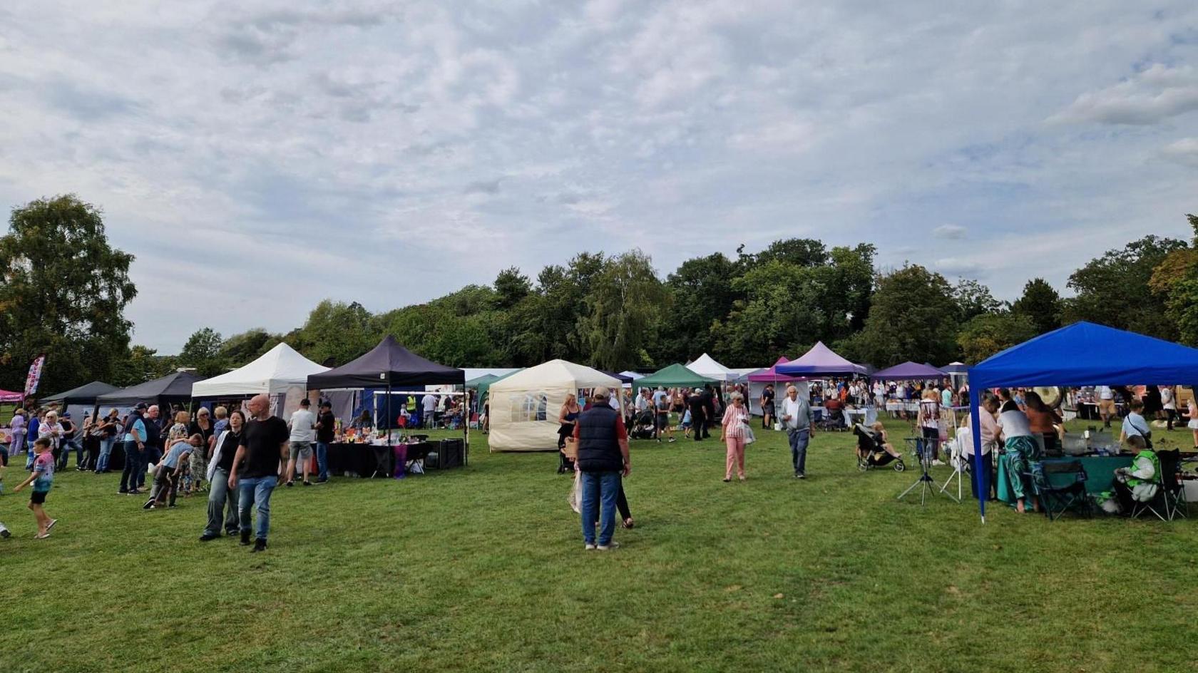 Different colour tents and gazebos to cover stalls - and people walking around in a small field