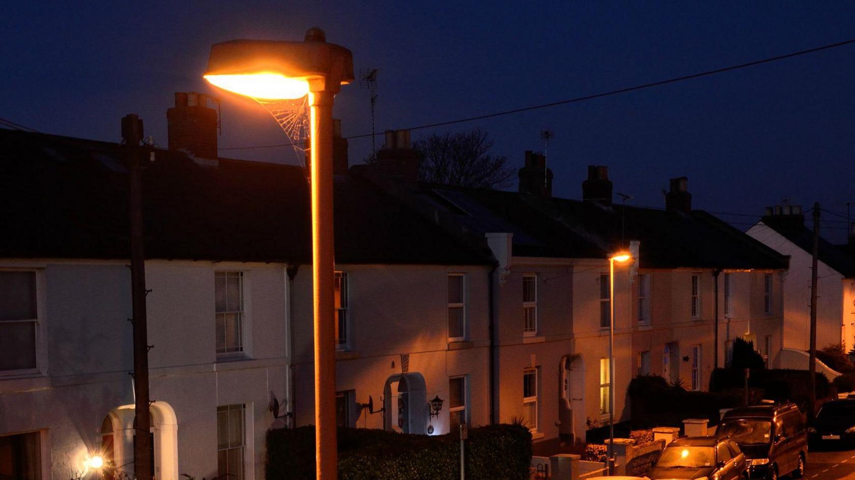A streetlight glows orange on a street at night.