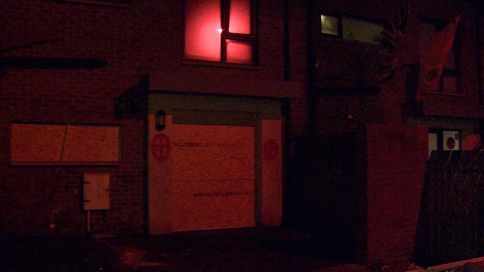 The picture, taken in darkness, shows the boarded up windows of a house with what are either cross-heads or cross symbols painted on the walls