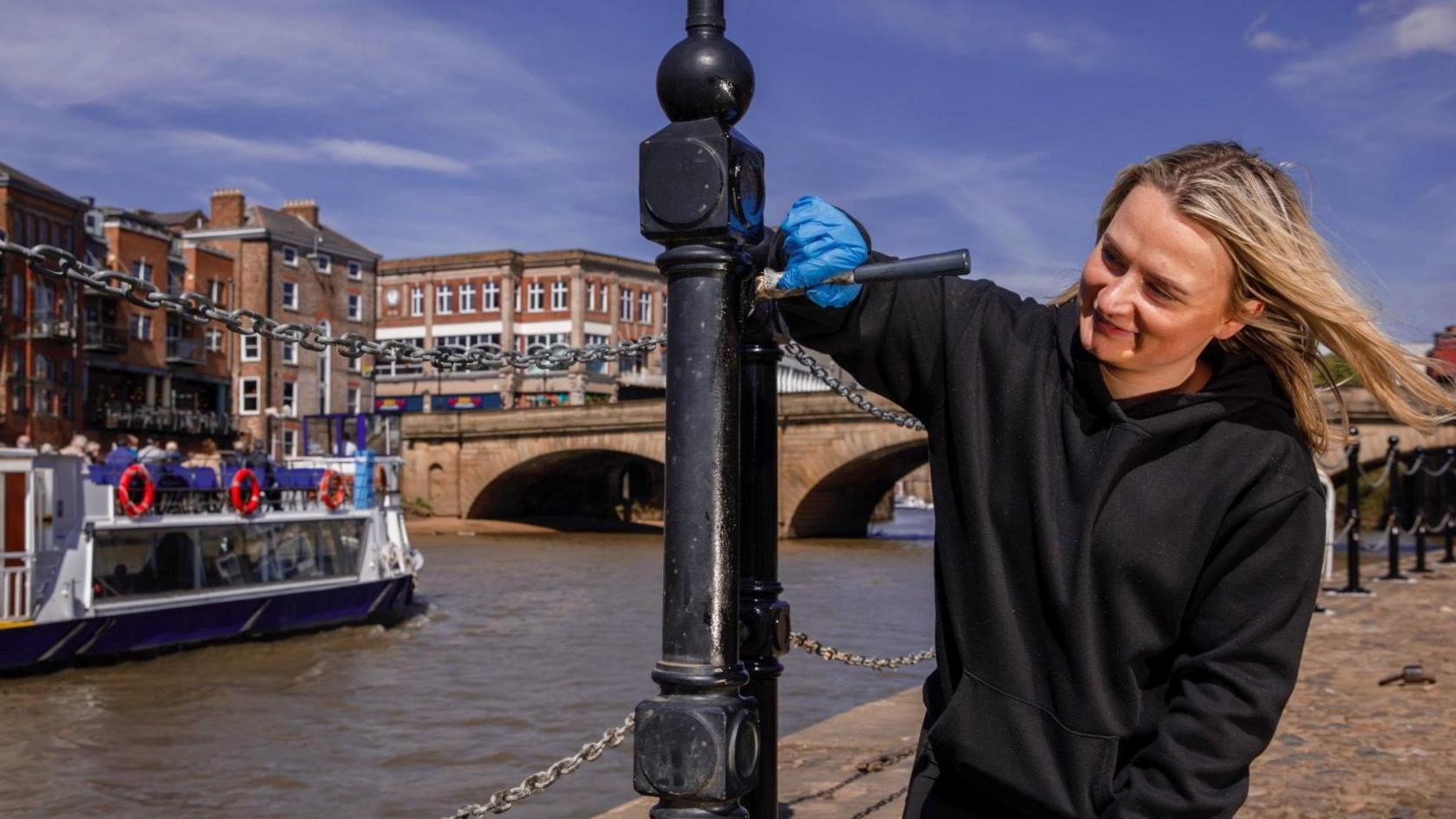 A volunteer painting bollards by the river.