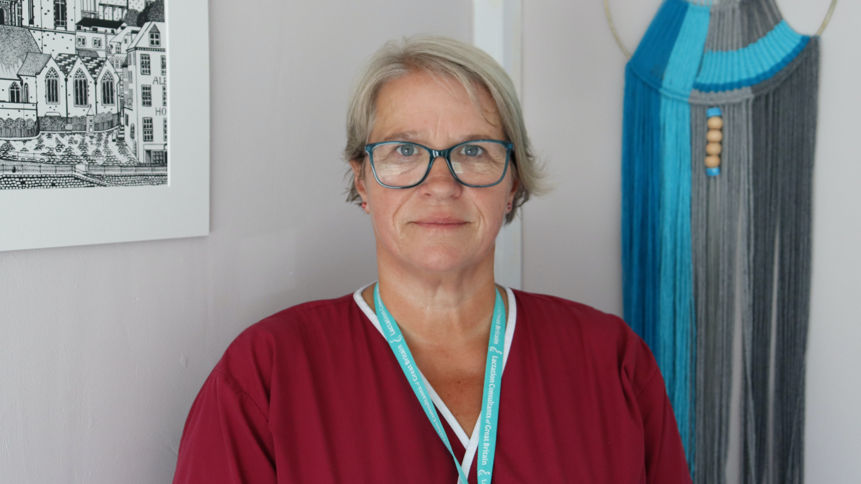 Jo Ingrouille in maroon medical scrubs, looking at the camera