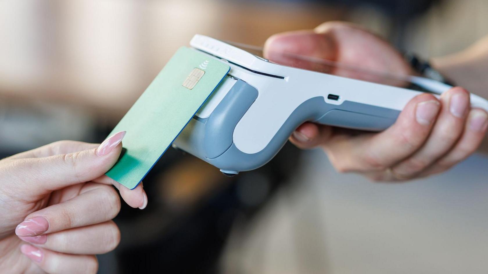 A woman taps her green credit card on a wireless payment terminal 