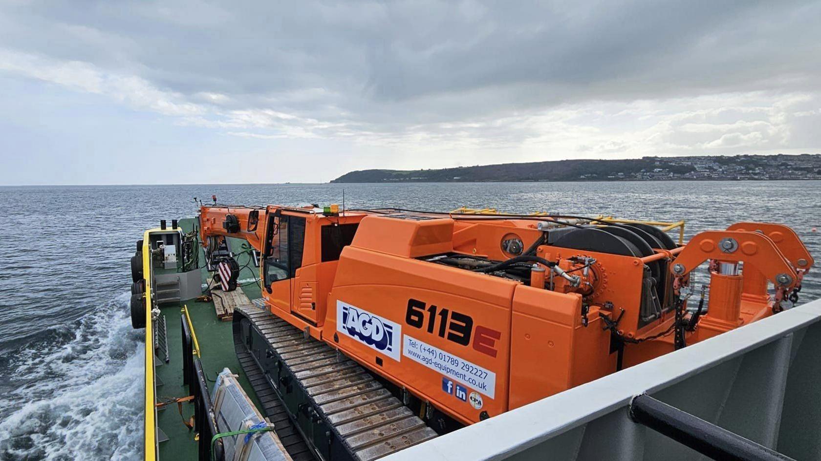 The crane is folded down on a boat in the sea with land in the background