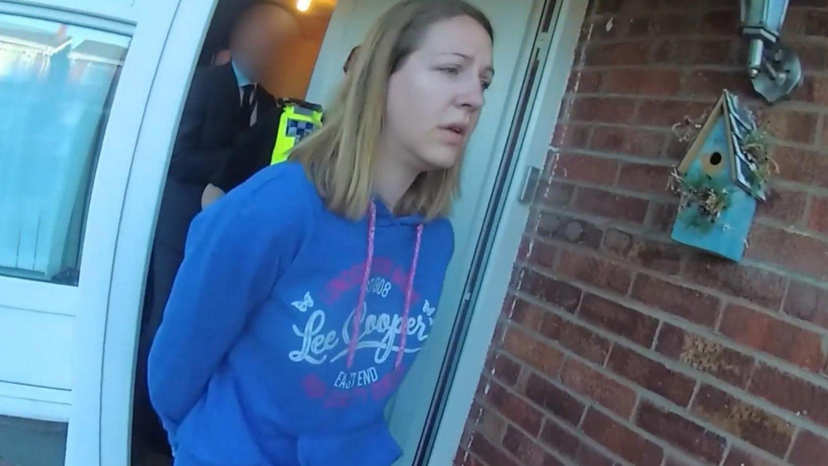 Lucy Letby, wearing a blue Lee Cooper brand hoodie, is led from her home in handcuffs 